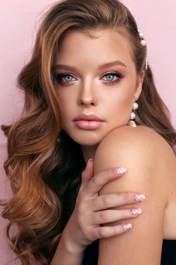 A woman with long hair and pearls on her shoulder.